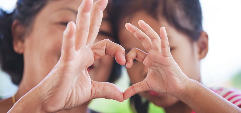 a mom and son handing hands and making a heart shaped gesture with their fingers.