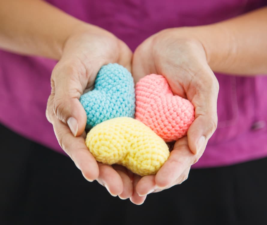 person holding 3 little knitted hearts, hands are cupped as actioning to hand them out