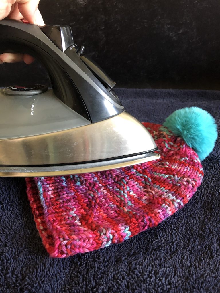 An iron hovers above a hat demonstrating how to steam block.