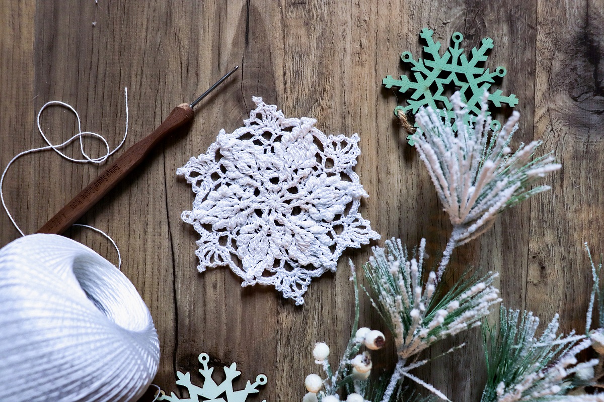 picture containing thread a crochet hook, pine needles, and knitted snow flake 
